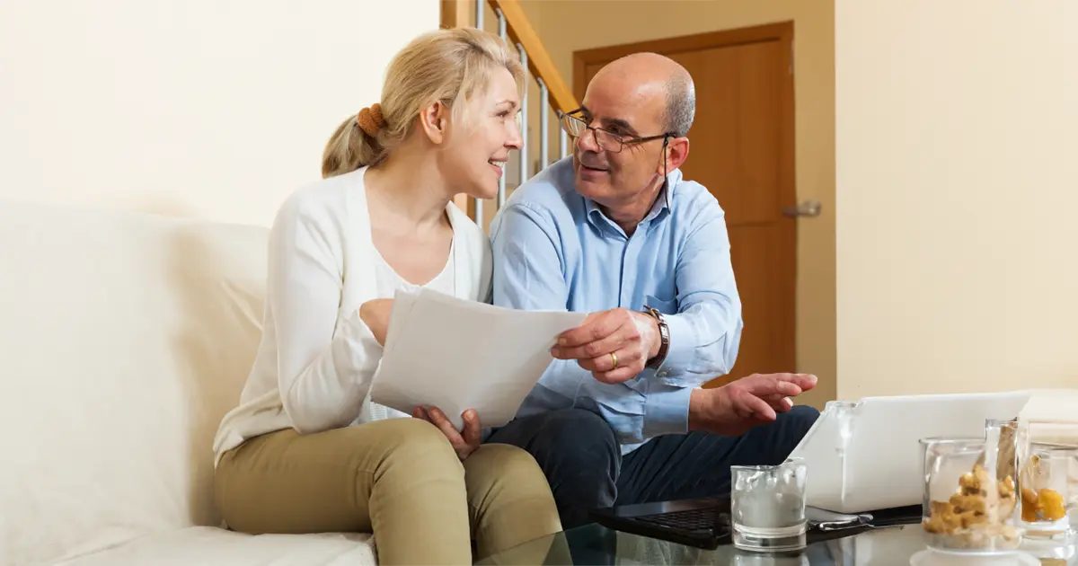 A couple sitting together holding a piece of paper and planning their retirement budget