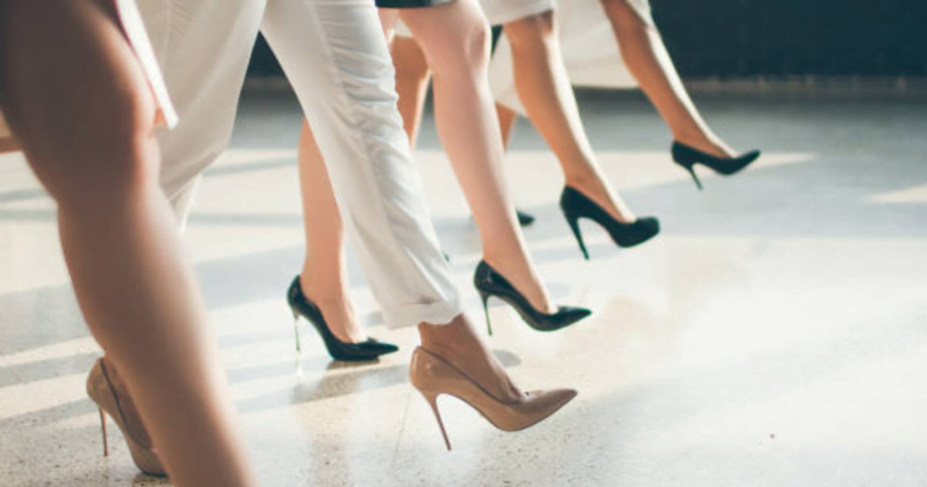 5 women stride in high heels, legs only are shown. 