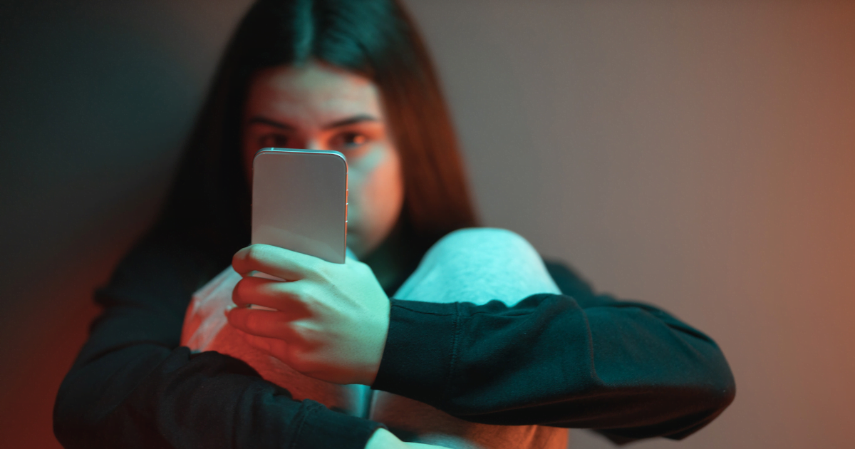 A young girl looks pensively at her mobile phone. 