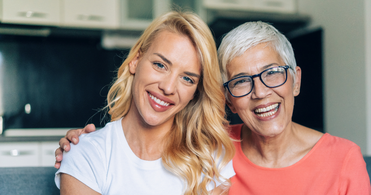 An older woman stands, smiling with a younger woman next to her. 