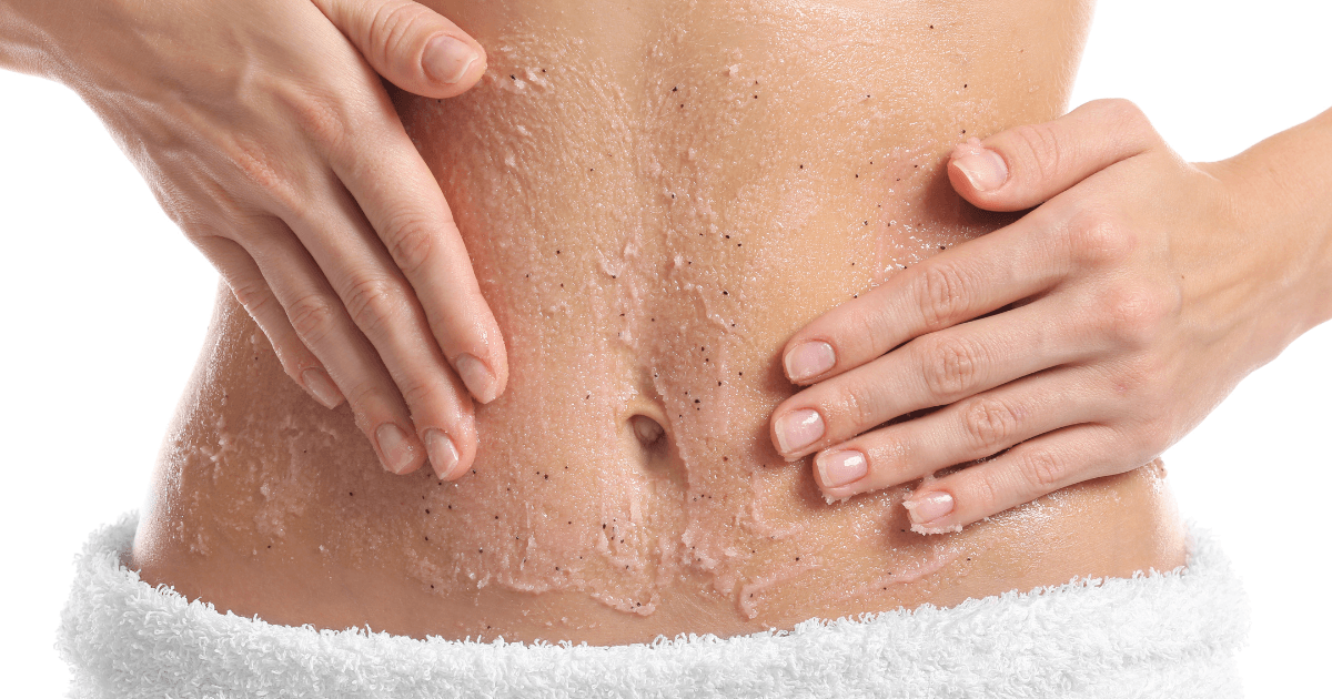 A woman applies a body scrub to her abdomen.