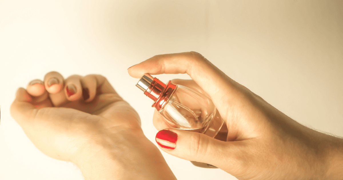 A woman sprays her wrist with a perfume bottle.