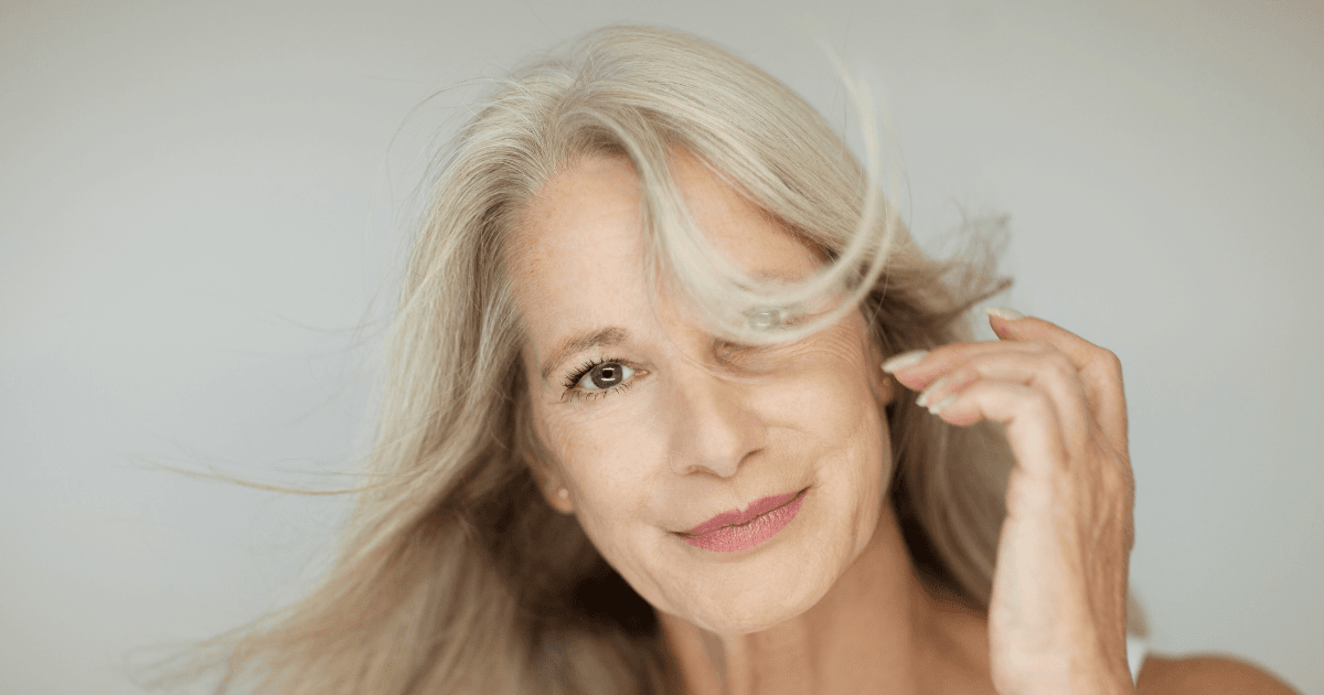 An older woman with blonde/grey hair smiling, fringe covering her eye